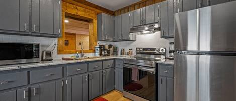 A modern kitchen with grey cabinets, stainless steel appliances, and wooden accents.