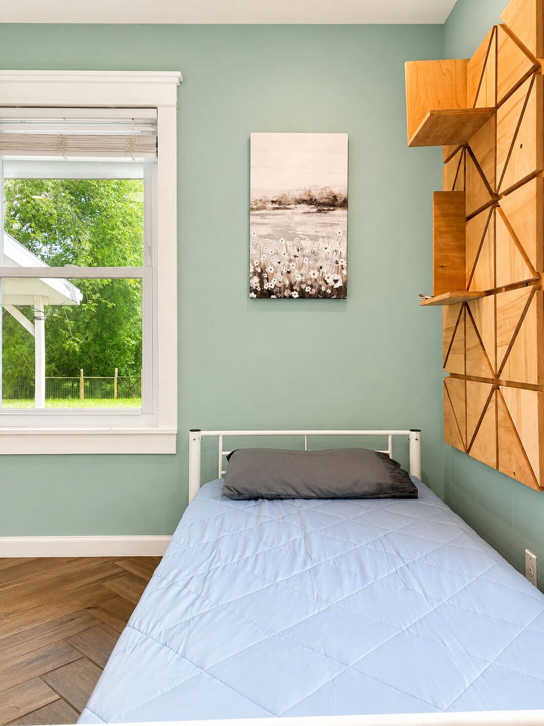 A bedroom with a bed, a window with blinds, a wall-mounted shelf, and a painting.