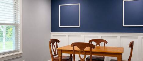 Un comedor con mesa y sillas de madera, ventilador de techo, iluminación empotrada y una ventana con persianas.