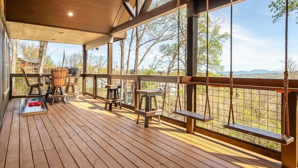 A wooden deck with outdoor seating, a table, and a view of trees and hills. - Sunset Above the Smokies (Gatlinburg)