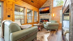 A log cabin interior with a stone fireplace, leather sofas, and large windows. - Sunset Above the Smokies (Gatlinburg)