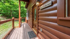 Una baita in legno con un cartello che riporta 'Sweet Fantasy', un'area prendisole in legno e uno sfondo boschivo.