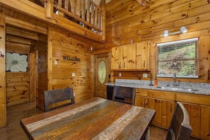 A wooden cabin interior with a dining table, chairs, a kitchen area, and a 'WELCOME' sign. - Sweet Fantasy (Sevierville)