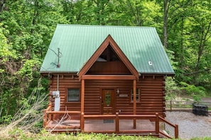 A log cabin with a green metal roof, a wooden front porch, and a fenced deck area. - Sweet Fantasy (Sevierville)