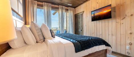 A wooden-paneled bedroom with a bed, curtains, a mounted TV, and a window.