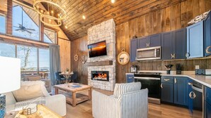 Una sala de estar acogedora con chimenea de piedra, televisor y una zona de cocina con armarios azules y microondas.