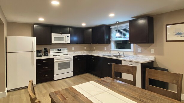 A modern kitchen with dark cabinets, a white refrigerator, a microwave, a stove, and a sink. - Close to the Causeway! (Naples)