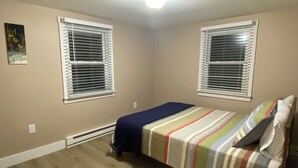 A bedroom with two windows, a bed with a striped bedspread, and a ceiling light. - Close to the Causeway! (Naples)