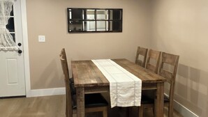 A dining area with a wooden table, four chairs, a white tablecloth, a mirror on the wall, and a door with a lace curtain. - Close to the Causeway! (Naples)