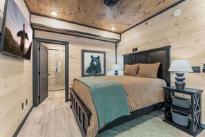 A wooden-paneled bedroom with a bed, two bedside lamps, a framed bear picture, and a door leading to another room. - Timber & Stone (Sevierville)