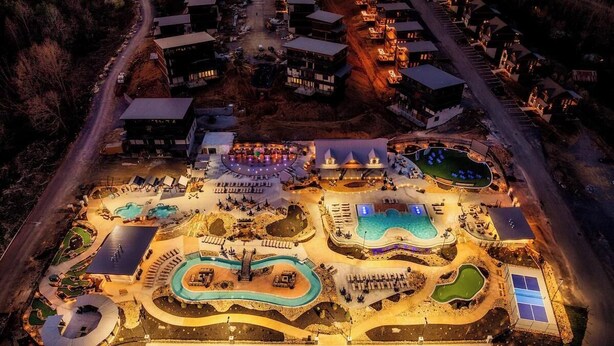 Eine Luftaufnahme eines Resorts mit mehreren Schwimmbecken, einer zentralen Bühne und verschiedenen Gebäuden.