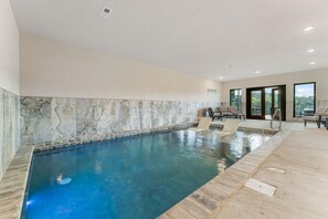 A swimming pool with a tiled wall, a seating area with chairs, and large windows. - Timber & Stone (Sevierville)