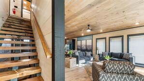 Eine Treppe mit Holzboden führt zu einem Wohnbereich mit Sofa, Couchtisch und Blick ins Freie.