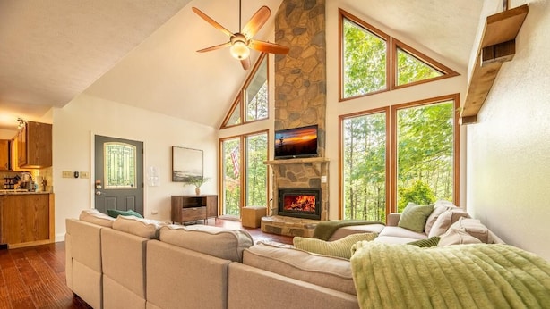 A spacious living area with a stone fireplace, large windows, and a ceiling fan. - Family Mountain Lodge (Sevierville)