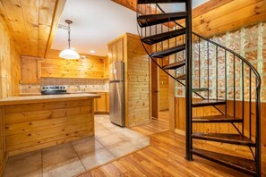 Ein Holzinnenraum mit einer Küche, einer zentralen Kochinsel, einer Wendeltreppe und einem Fliesenboden.