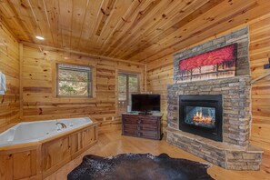 Ein rustikaler Blockhaushof mit Kamin aus Naturstein, einem großen Fenster und einer Holzbadewanne.
