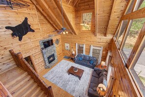 Ein Interieur einer Blockhütte mit Kamin, einer Couch, einem Couchtisch und einem Fellteppich.