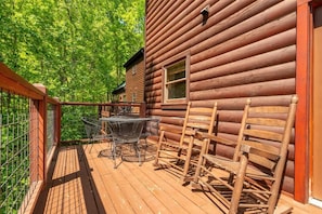 A wooden deck with a table and chairs, a metal railing, and a log cabin building. - Paradise Found (Sevierville)