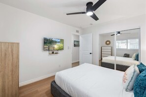 Ein Schlafzimmer mit einem Bett, einem Deckenventilator, einem an der Wand montierten Fernseher und einer Tür zu einem anderen Raum.