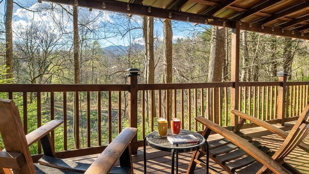 Una terraza de madera con una mesa y sillas, con vista a un área boscosa y montañas a lo lejos.
