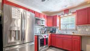 Una cocina con gabinetes rojos, electrodomésticos de acero inoxidable, microondas, horno y refrigerador.