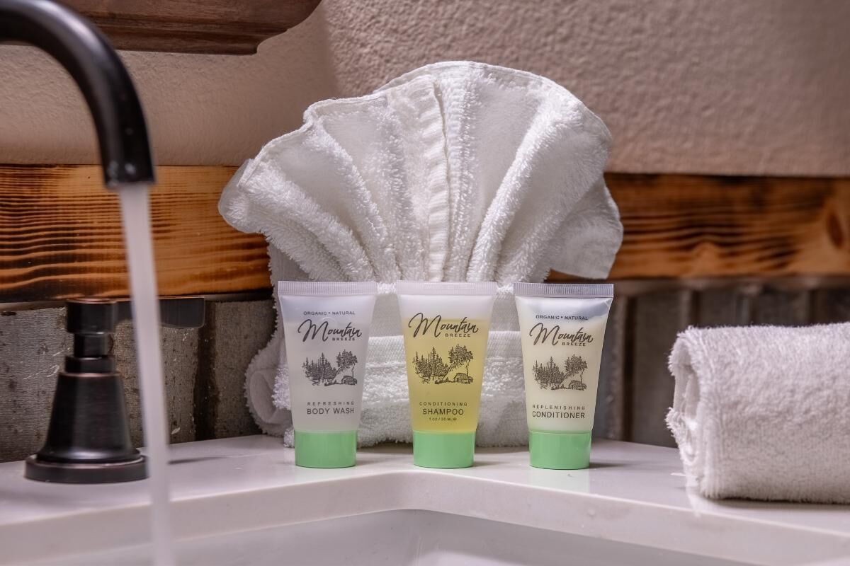 Ein Waschbecken mit drei Mountain Duschgels und Spülungen, einem weißen Handtuch und einer Duschbrause.