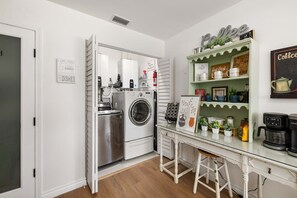 A compact kitchen with a built-in washer and dryer, a coffee station, and a small dining area with stools. - Luxury 3BR Retreat | Hot Tub, Fire Pit & Games (Simi Valley)