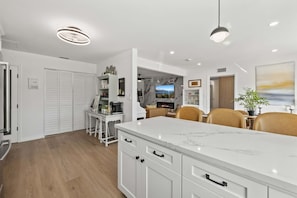 A modern kitchen with white cabinetry, a marble countertop, and a dining area with a white table and chairs. - Luxury 3BR Retreat | Hot Tub, Fire Pit & Games (Simi Valley)