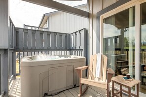 Ein Whirlpool auf einer Holzterrasse mit einem Stuhl, einem Tisch, einer Glastür und einem weißen Gebäude im Hintergrund.