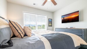 A bedroom with a bed, a ceiling fan, a window with blinds, a TV on the wall, and a dresser. - All We Need (Sevierville)