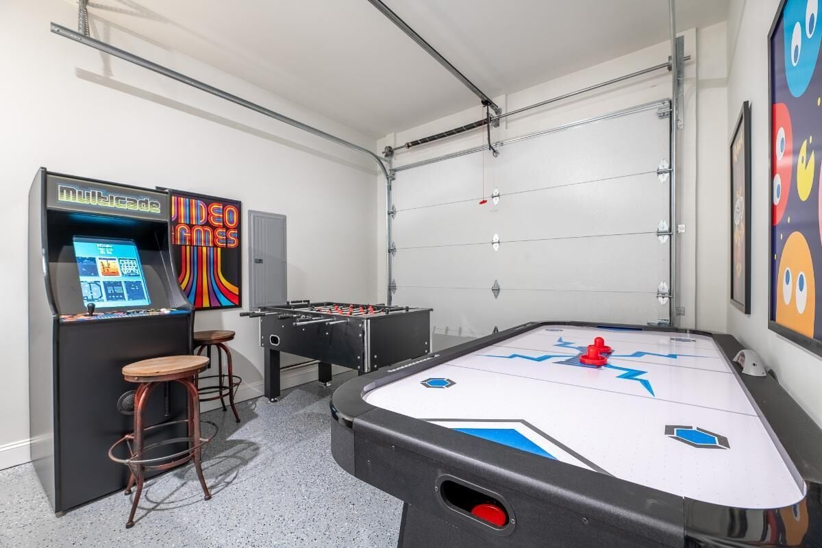 A room with a foosball table, a video game machine, and two stools.