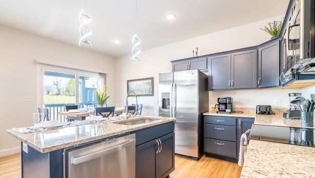 A modern kitchen with a central island, stainless steel appliances, dark cabinetry, and a view to the outdoors. - All We Need (Sevierville)