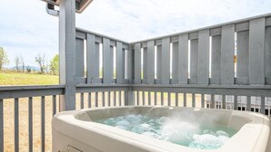 A hot tub in an outdoor setting with a wooden deck and a view of the landscape. - All We Need (Sevierville)