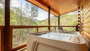 Un bain à remous sur une terrasse en bois, avec vue sur une zone boisée.