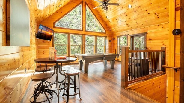 L’intérieur d’un chalet en bois, avec une table de billard, des tabourets de bar et de grandes fenêtres.