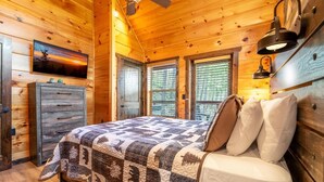 Une chambre dans une cabane en bois, avec un lit, une commode, une télévision et des fenêtres.