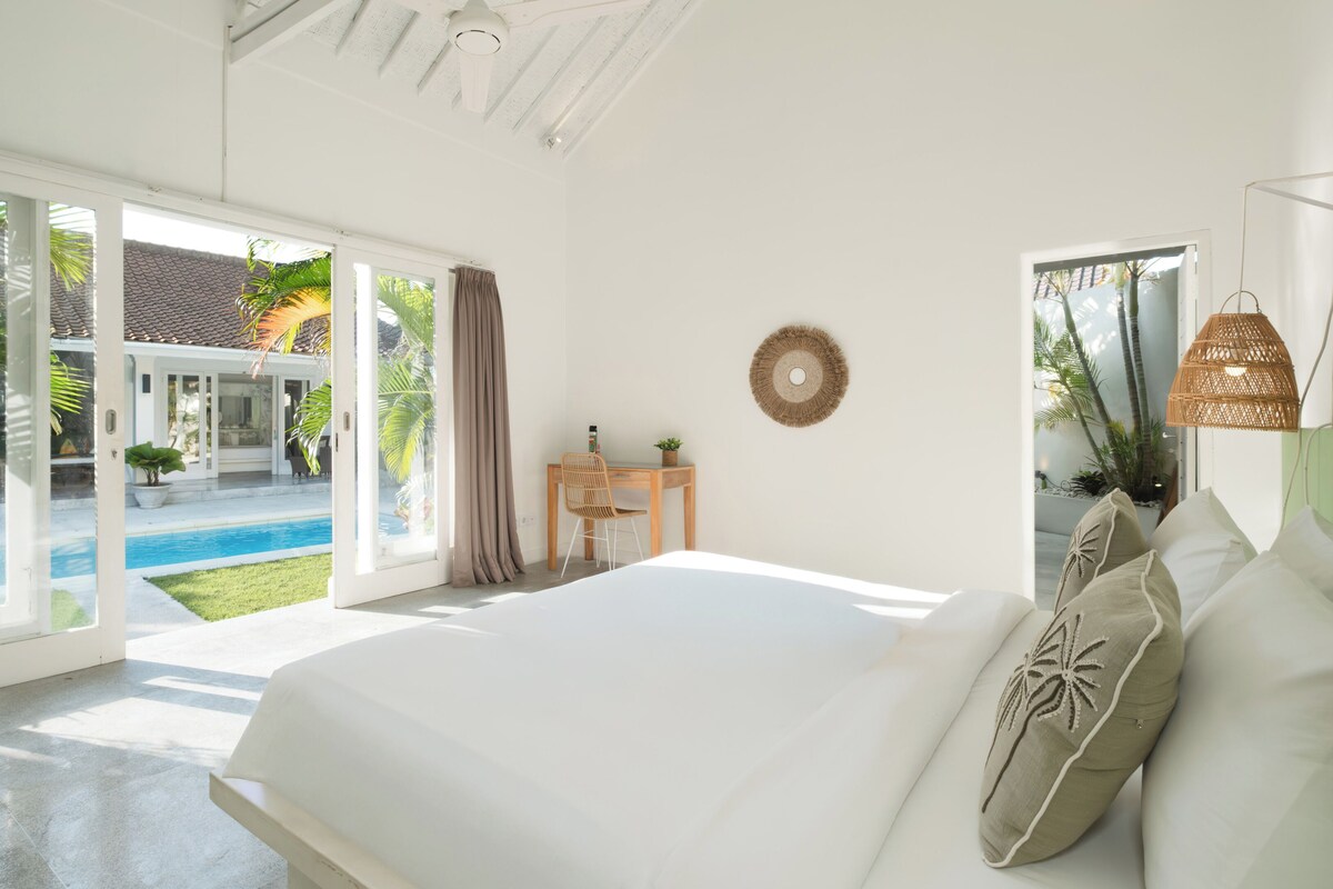A bedroom with a large bed, a desk, and a view of a swimming pool.