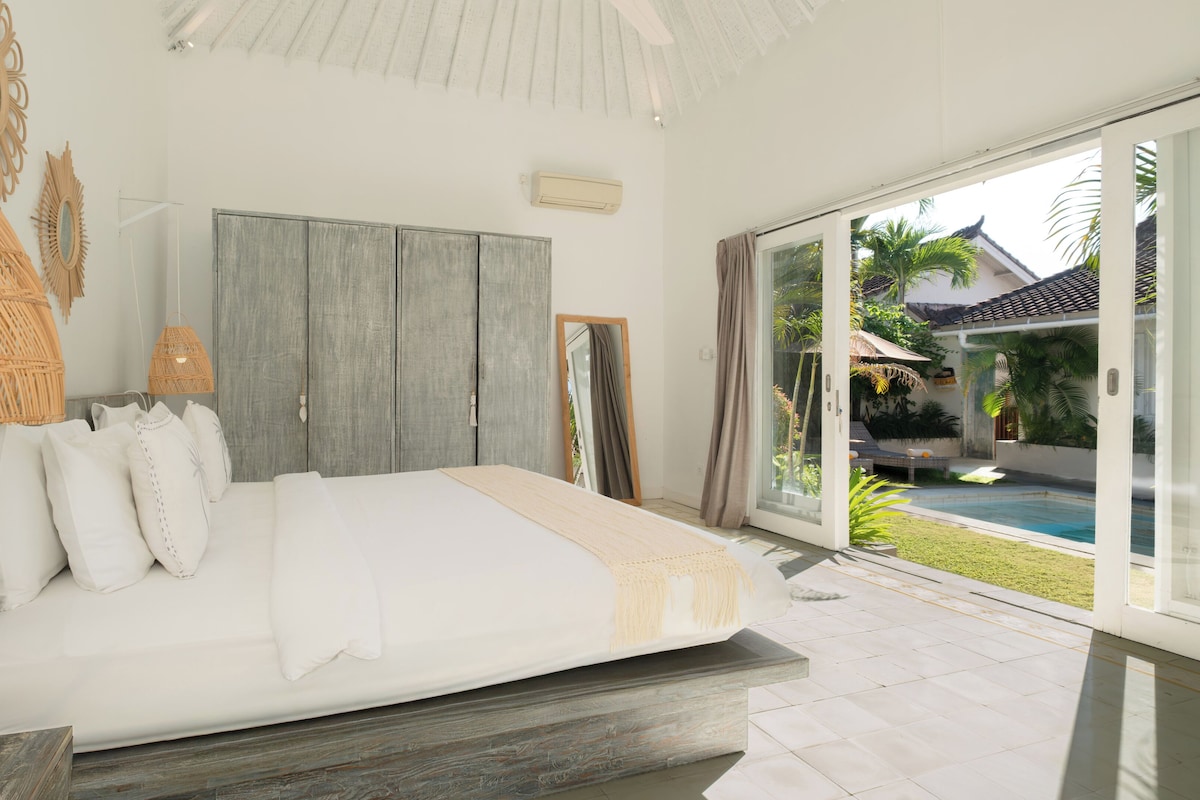 A bedroom with a large bed, a wardrobe, a mirror, and a view of a swimming pool.