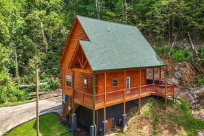 A wooden cabin with a green roof, a porch, and a view of the surrounding forest. - Z - Smoky Serenity Retreat (Sevierville)