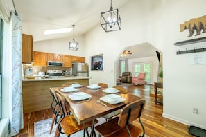 A dining area with a wooden table set for four, a kitchen with wooden cabinets, a microwave, and a stove, and a ceiling fan. - Little Cub Cottage (Gatlinburg)