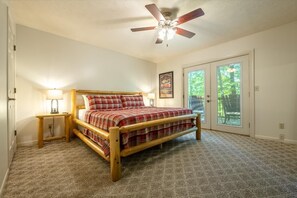 A bedroom with a wooden bed, a ceiling fan, a nightstand, and a window with blinds. - Little Cub Cottage (Gatlinburg)