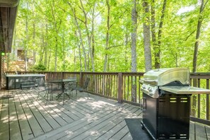 A deck with a grill, outdoor seating, and a view of a forest. - Little Cub Cottage (Gatlinburg)