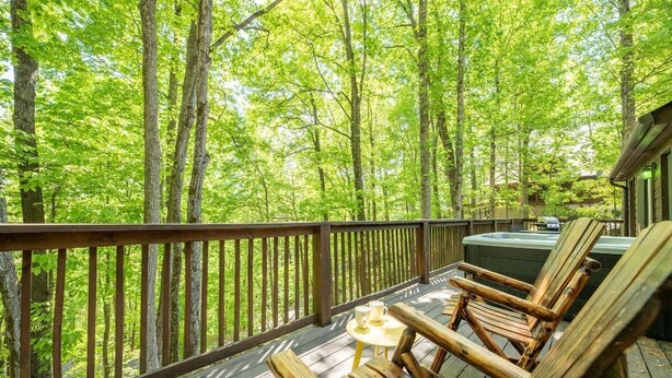 Um deck de madeira com uma banheira de hidromassagem, cadeiras de lounge e vista para uma floresta.