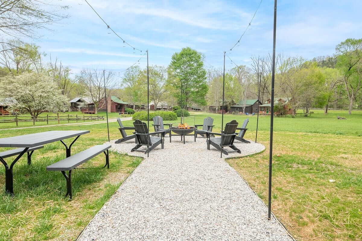 An outdoor seating area with tables and chairs, a fire pit, and a gravel path leading to a building.