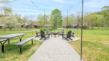 An outdoor seating area with tables and chairs, a fire pit, and a gravel path leading to a building.