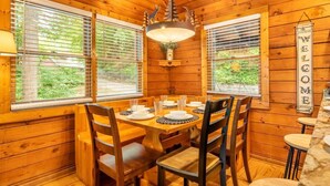 A wooden cabin interior with a dining table set for four, a hanging light fixture, and a 'WELCOME' sign. - Lofty Pines (Sevierville)