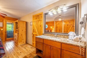 A wooden cabin-style bathroom with a large mirror, granite countertop, wooden cabinets, and a hairdryer. - Lofty Pines (Sevierville)