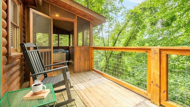 A wooden deck with a table and chairs, a covered seating area, and a view of the surrounding forest. - Lofty Pines (Sevierville)