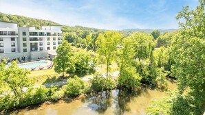 A modern hotel with a swimming pool, surrounded by lush greenery and a river. - The Bears Den (Pigeon Forge)