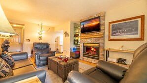 A cozy living room with leather sofas, a fireplace, and a television mounted on a stone wall. - The Bears Den (Pigeon Forge)